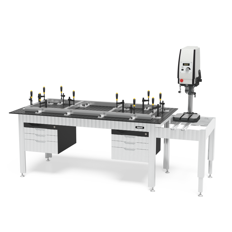 Load image into Gallery viewer, Siegmund welding table with a perforated tabletop, clamp squares and stops set up along a long fixture frame, drawer cabinets underneath, and a press or tapping unit mounted on a side extension table.
