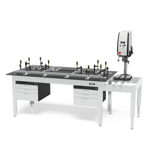 Siegmund welding table with a perforated tabletop, clamp squares and stops set up along a long fixture frame, drawer cabinets underneath, and a press or tapping unit mounted on a side extension table.